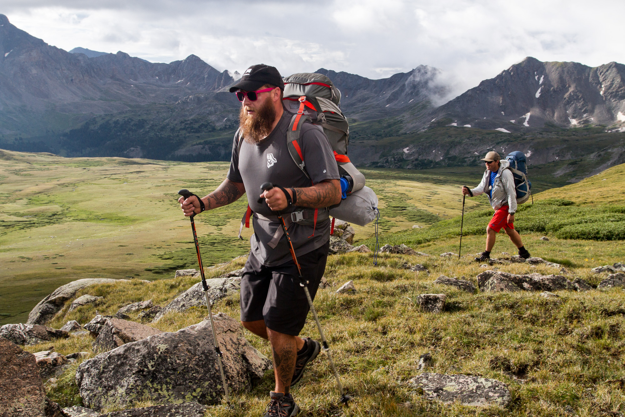 man hiking with walking poles, with pink sunglasses and beard